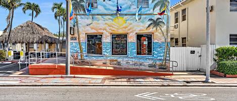 A building with a mural of a beach scene, a sign for Hollywood Beach Hotels, and a bicycle lane symbol on the road.