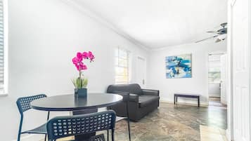 Una sala de estar moderna con una mesa redonda, dos sillas, un sofá y una orquídea en maceta.