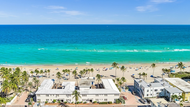A beachside hotel with a view of the ocean, palm trees, and beachgoers. - Hollywood Beach Blue Wave (Hollywood)