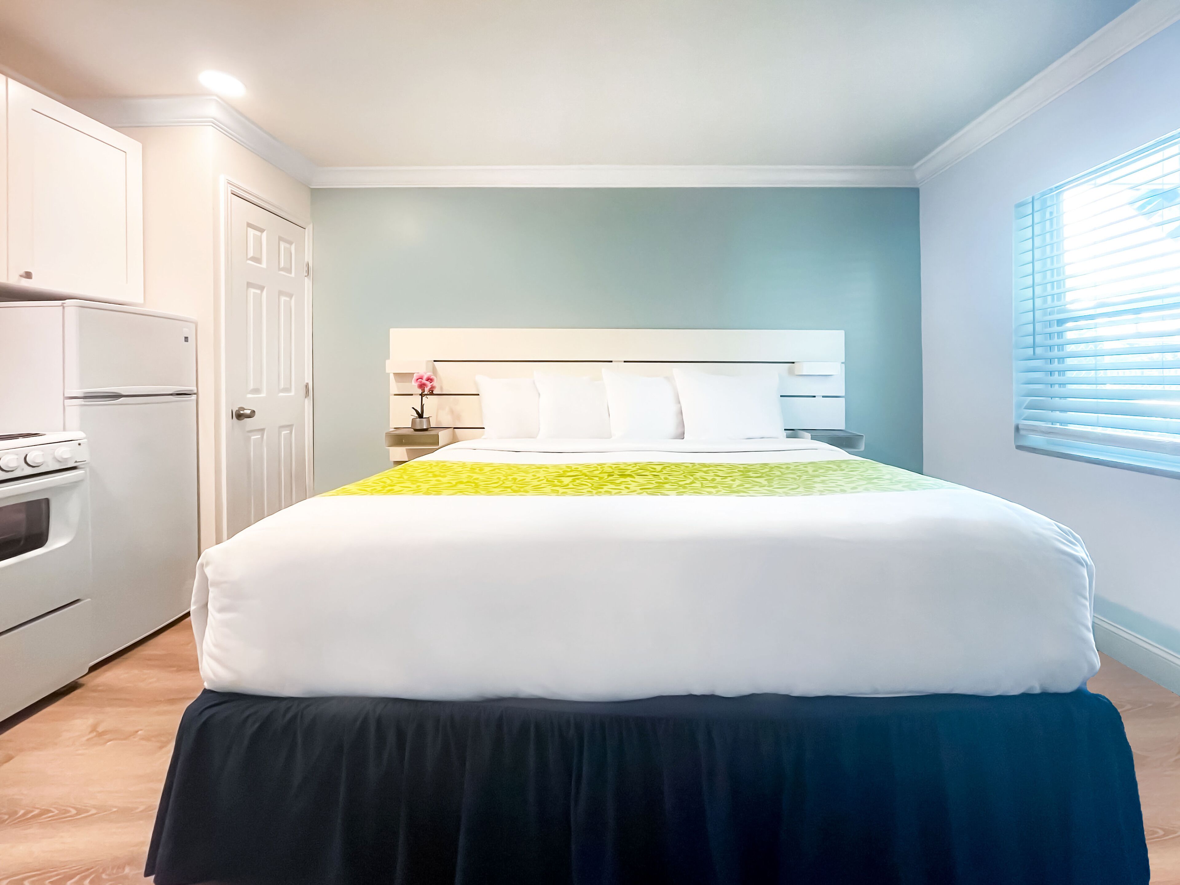 A bedroom with a bed, a nightstand, a dresser, and a window with blinds.