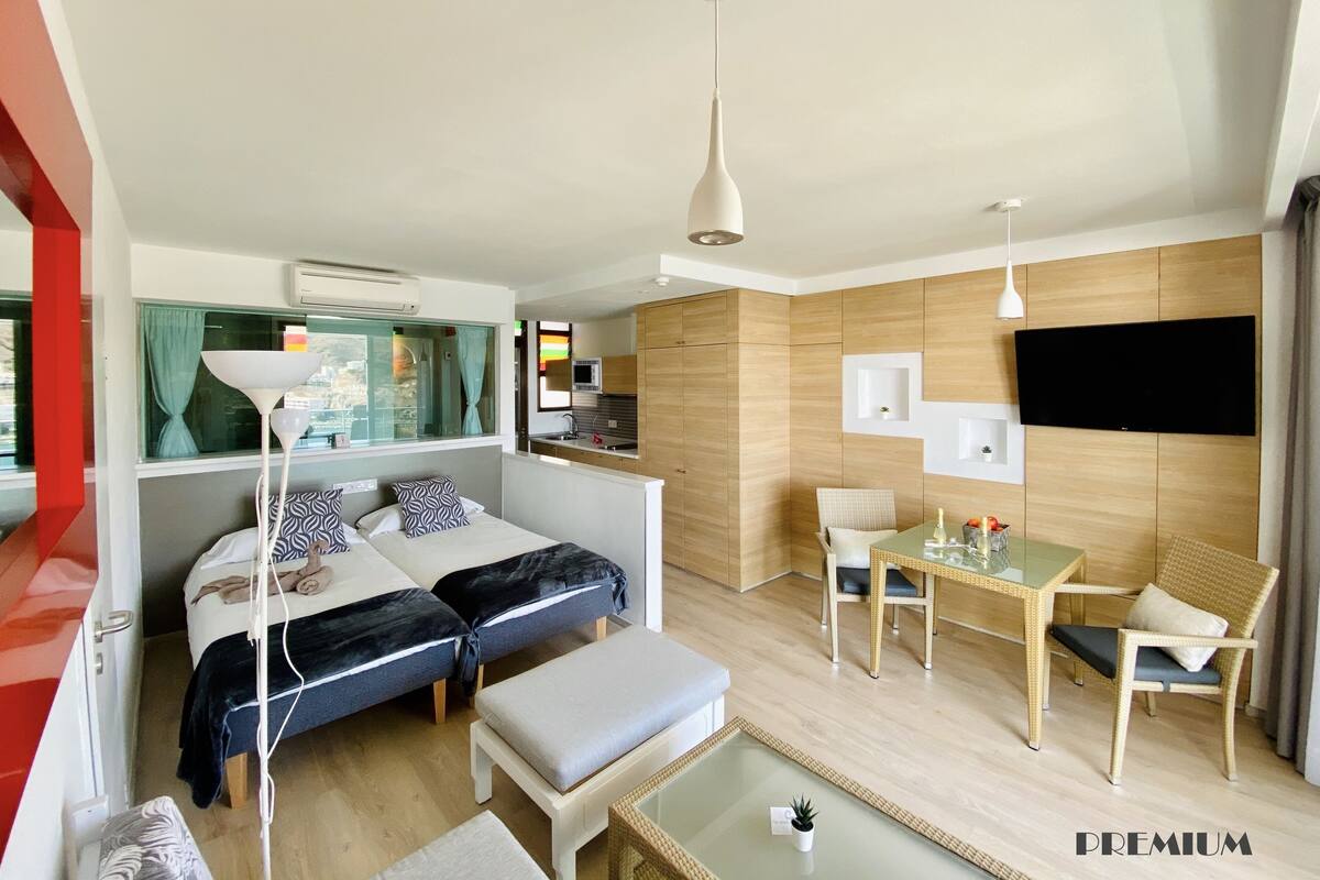 A modern hotel room with a bed, a dining area, and a TV.