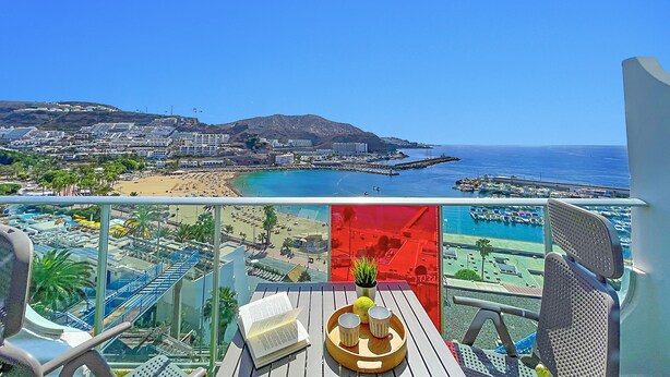 Un balcon avec vue sur une plage, une jetée et un paysage montagneux.