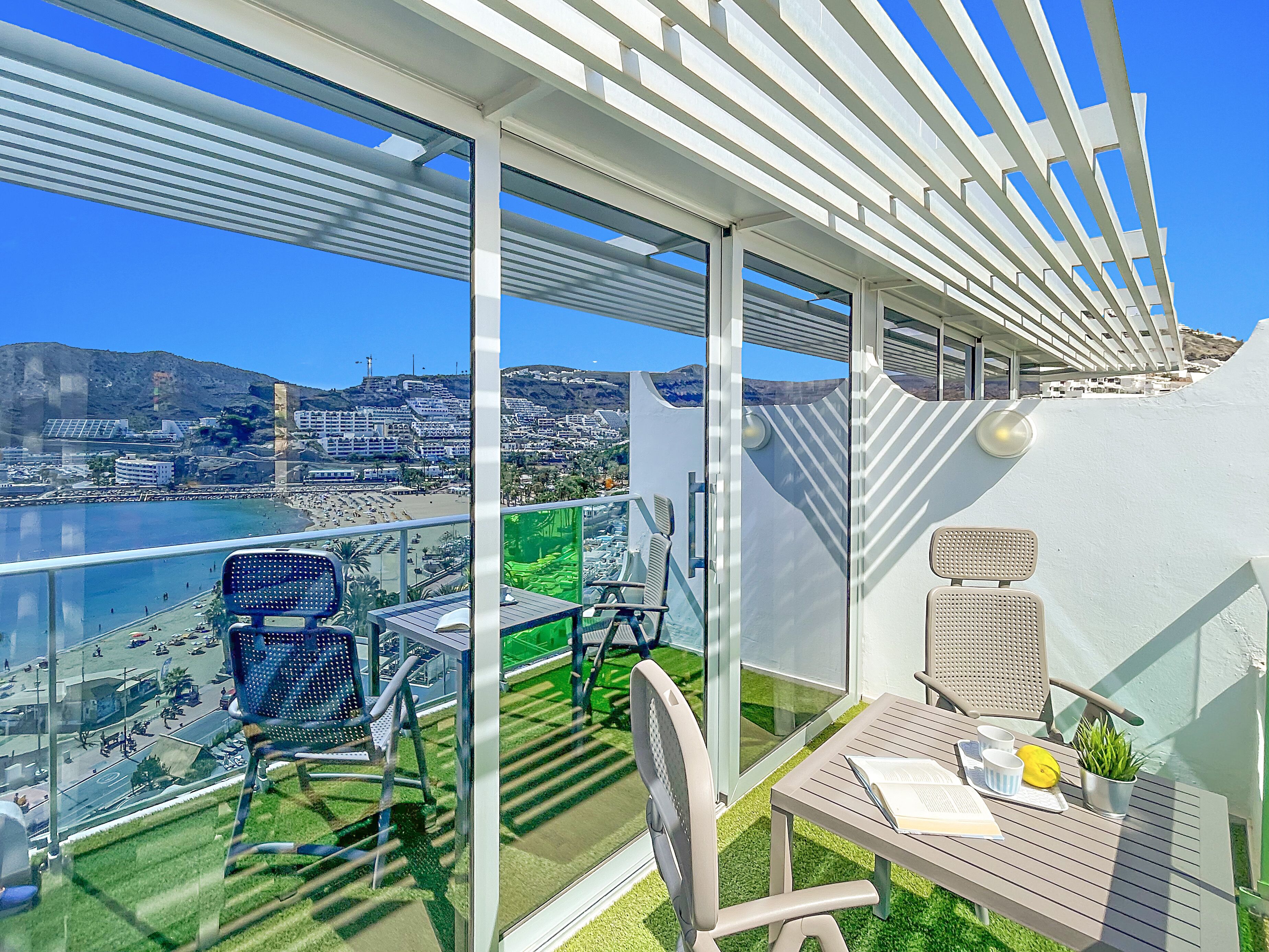 A balcony with a view of a beach and cityscape, furnished with chairs and a table.