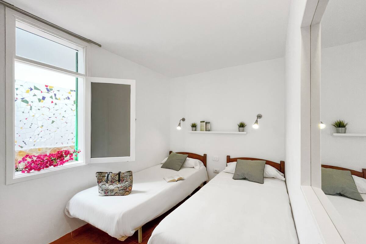 Un dormitorio con dos camas individuales, una ventana con vistas y una estantería con adornos.