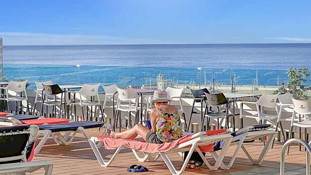 A sunny outdoor seating area with white plastic chairs and tables, overlooking a calm sea. - Porlamar (Mogan)