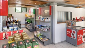 A store interior with shelves stocked with various products, a refrigerated display case, and a wooden ceiling. - Porlamar (Mogan)