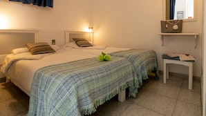 A hotel room with two beds, a bedside table, a mirror, and a shelf with a handbag. - Porlamar (Mogan)