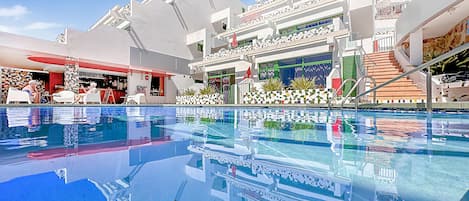 A modern hotel with a swimming pool, outdoor seating, and a bar area.