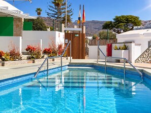 Une piscine aux carreaux bleus d’une couleur vive, entourée d’un bâtiment blanc doté d’une porte en bois et d’une enseigne indiquant la mention « SORTIE ».