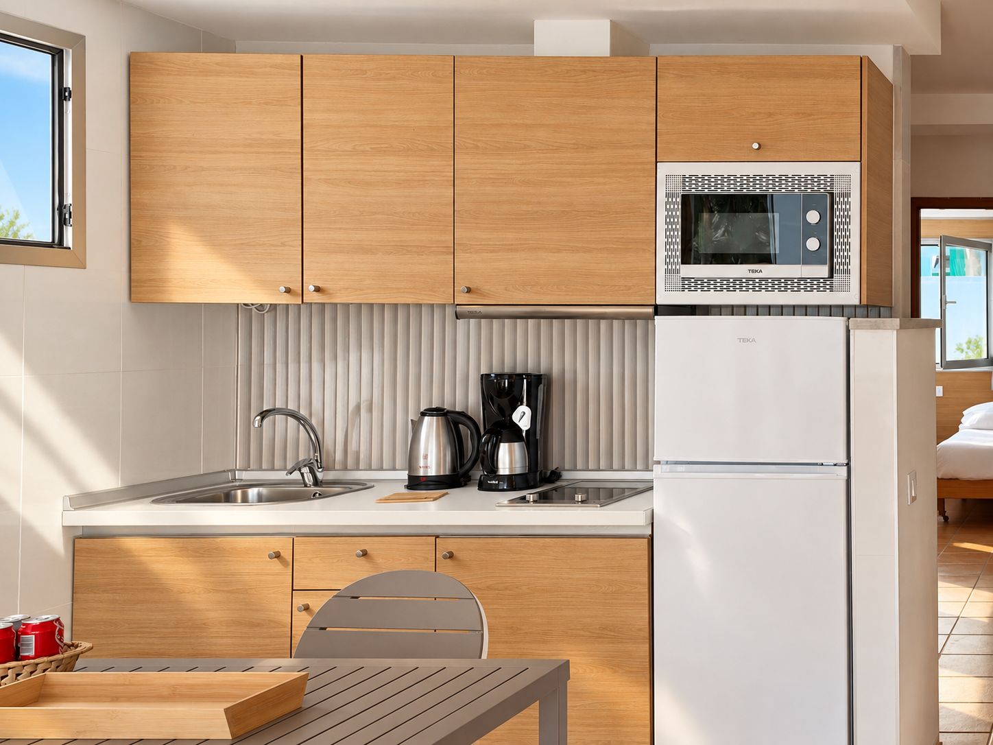 A modern kitchen with wooden cabinets, a stainless steel sink, a kettle, a coffee maker, and a white refrigerator.