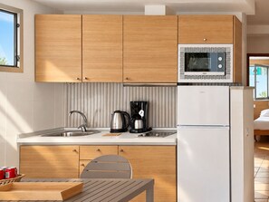 Une cuisine moderne avec des meubles en bois, un évier en acier inoxydable, une bouilloire, une machine à café et un réfrigérateur blanc.