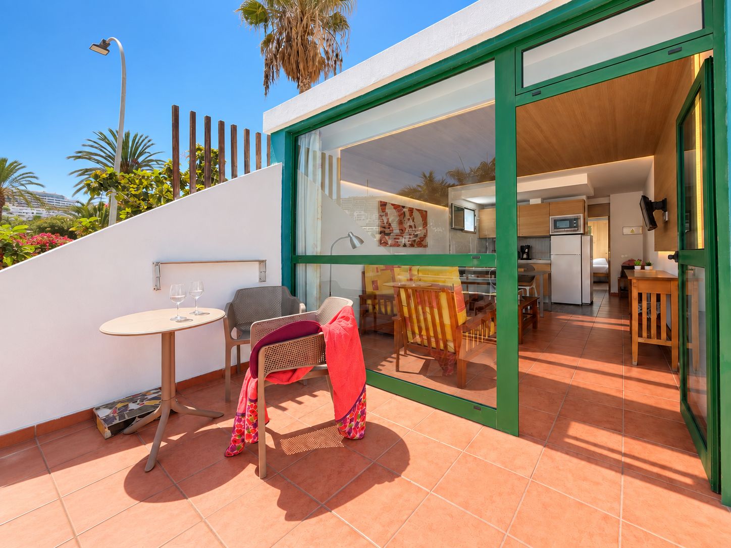 A modern outdoor patio with a dining area, a kitchen visible through glass doors, and a staircase leading to an upper level.