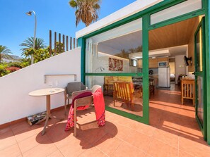 Une terrasse extérieure moderne comprenant un espace repas, une cuisine visible à travers des portes vitrées et un escalier menant à un niveau supérieur.