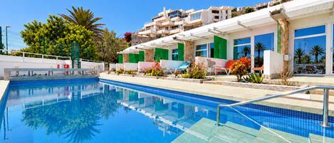 A swimming pool with clear blue water, surrounded by a poolside area with lounge chairs and potted plants.