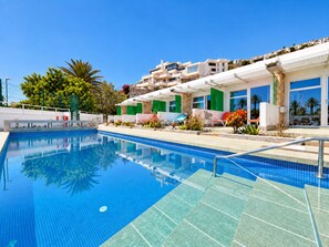 A swimming pool with clear blue water, surrounded by a poolside area with lounge chairs and potted plants. - Leticia Del Mar (Mogan)