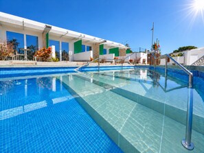 A clear blue pool with a tiled deck, surrounded by a building with large windows and a green accent wall. - Leticia Del Mar (Mogan)