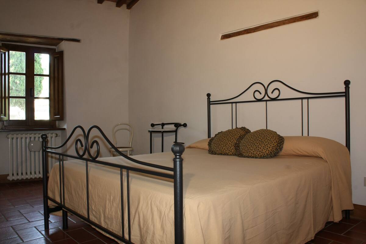 A single bed with a metal frame and beige bedding in a room with white walls and a window.