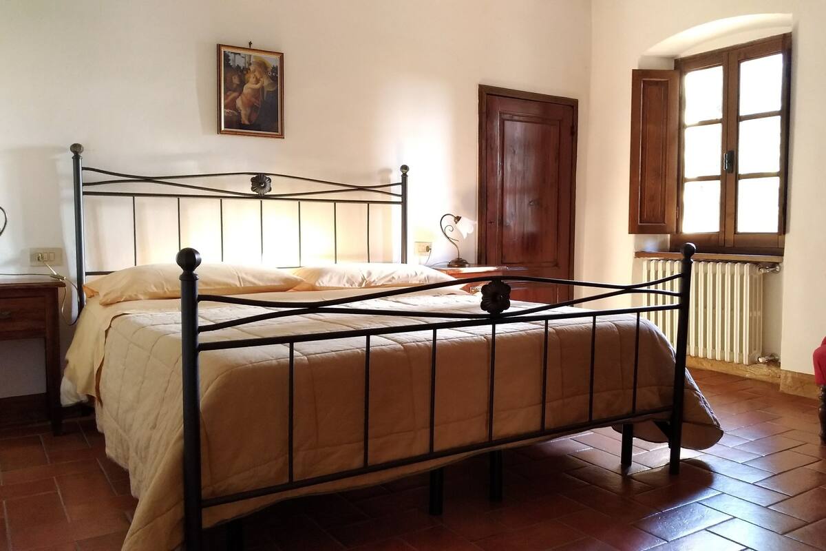 A bedroom with a metal bed frame, a wooden door, a radiator, and a window with a view.