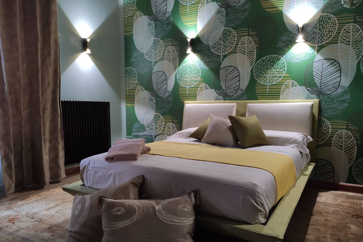 A neatly made bed with pillows and a folded towel, a headboard with a light fixture, and a green leaf-patterned wall.