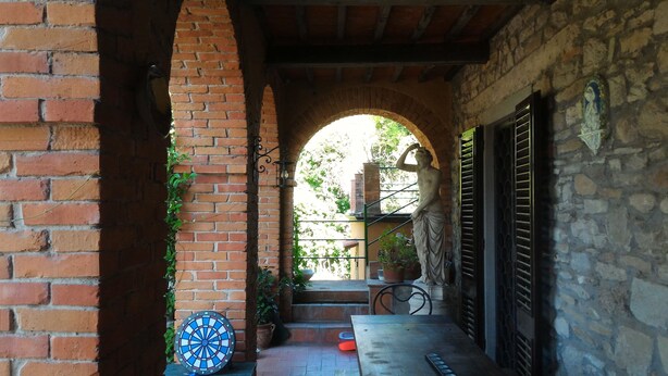 Un arco de ladrillo que da acceso a un patio con una estatua, un dardo y una bicicleta.