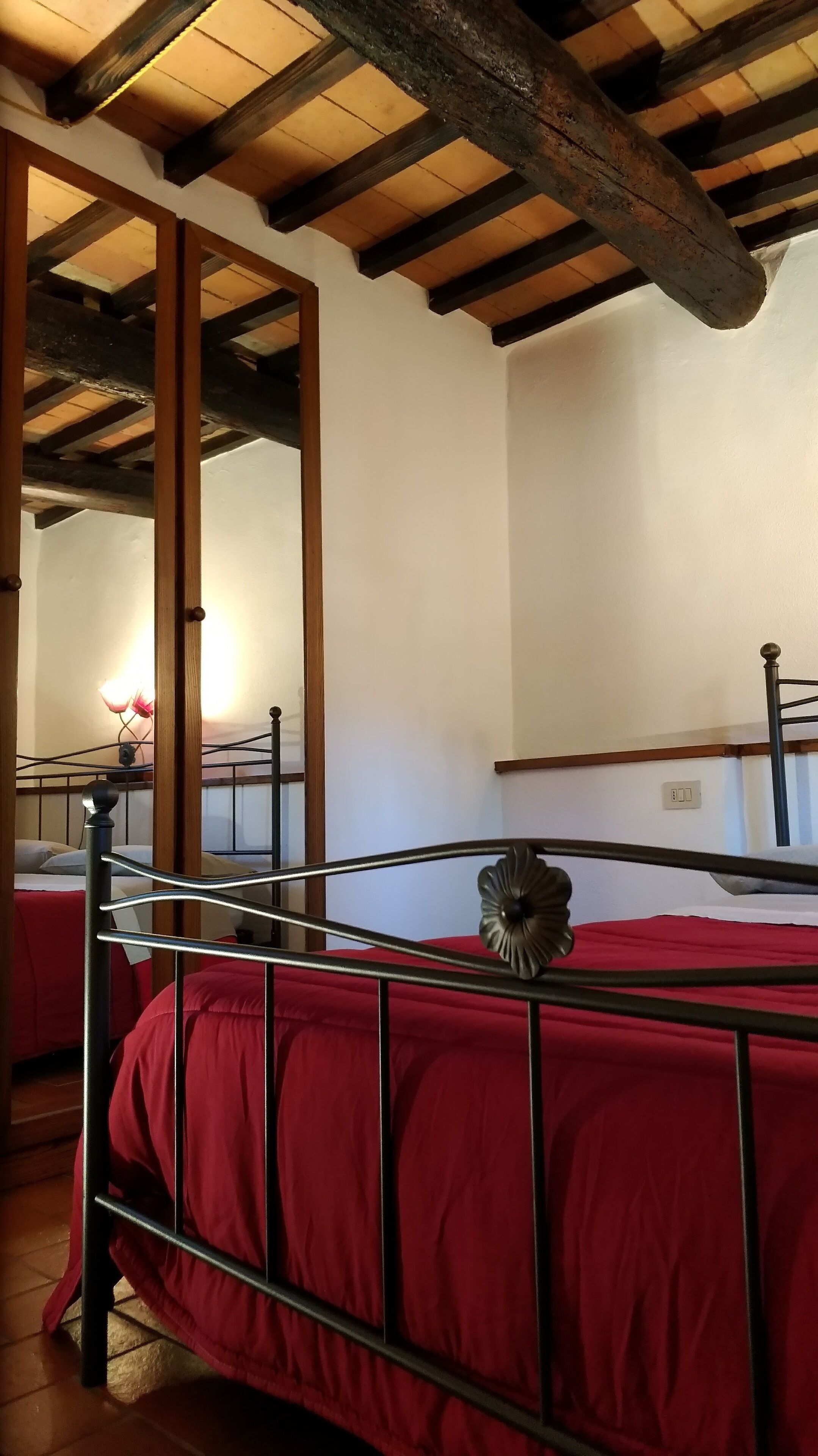 Un dormitorio con techo de madera, estructura de cama metálica y colcha roja.