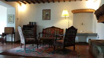 Una habitación con techo de madera, alfombra estampada, una silla de madera, una estantería y una lámpara de pared.