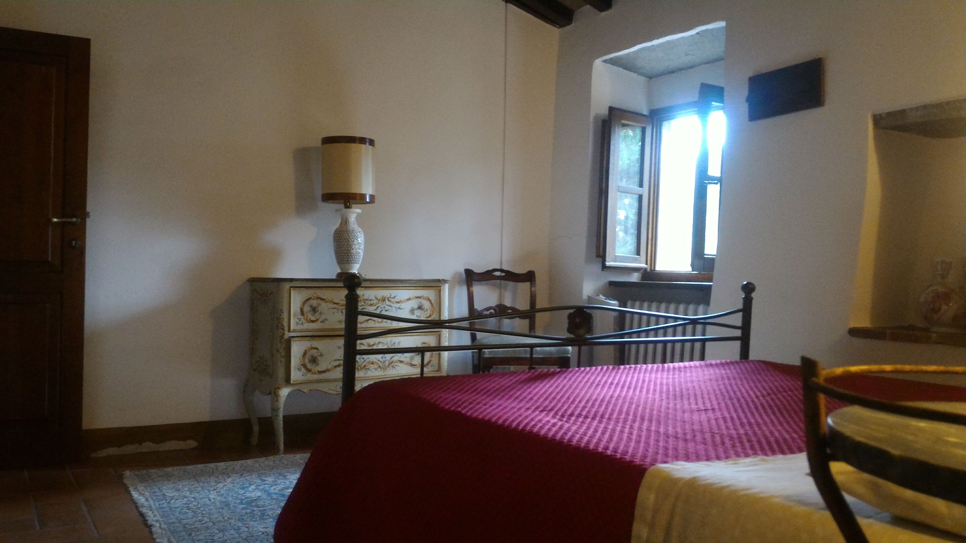 Ein Schlafzimmer mit Bett, Kommode, Stuhl, Lampe und Fenster.