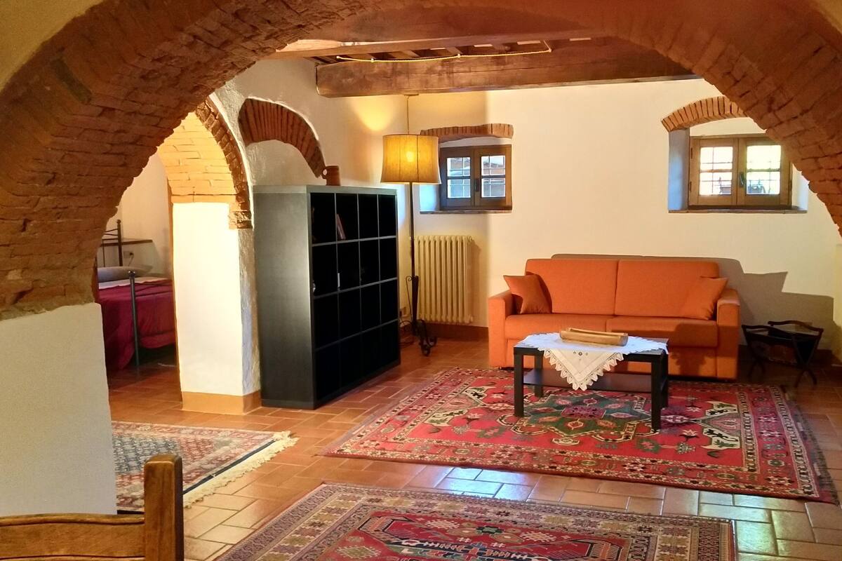 An interior with a brick archway, a sofa, a table with a cloth, and a radiator.