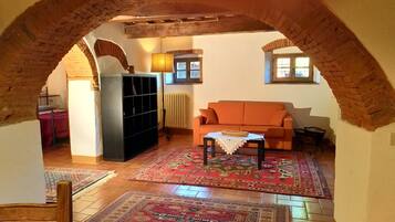An interior with a brick archway, a sofa, a table with a cloth, and a radiator.