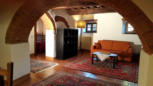 An interior with a brick archway, a black bookshelf, an orange sofa, and patterned rugs on a tiled floor. - B&B Villa La Nussa (Capolona)