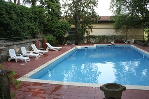 A rectangular swimming pool with a tiled edge, surrounded by white lounge chairs and potted plants.