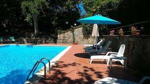 Una piscina rectangular con muro de piedra y solárium empedrado.