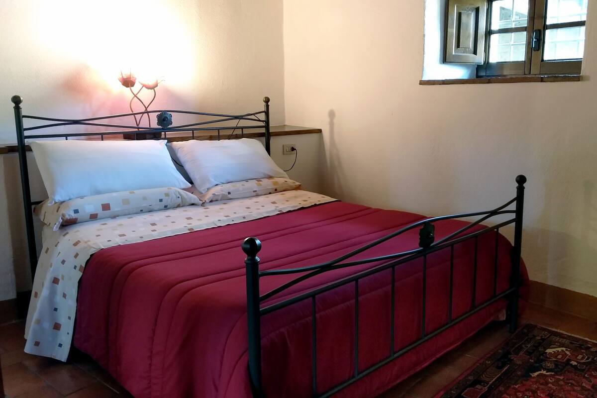 A bed with a metal frame, white and patterned bedding, and a red blanket.
