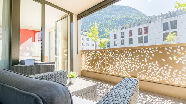 A balcony with wicker furniture, a view of buildings, and a decorative wall. - Centerpark Apartments (Visp)