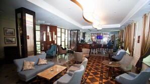 Un vestíbulo de hotel con zona de bar, arreglos de asientos y piso estampado.