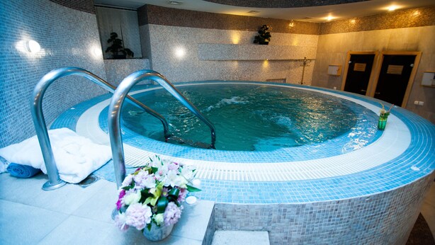 Un jacuzzi con borde de azulejos, una escalera metálica y un arreglo floral en el suelo.