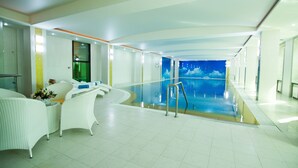 Una piscina interior moderna con vistas despejadas al agua, muebles de mimbre blanco y barandilla de vidrio.