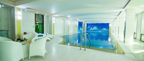 Una piscina interior moderna con vistas despejadas al agua, muebles de mimbre blanco y barandilla de vidrio.
