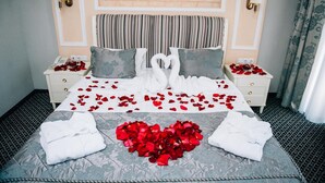 Una habitación de hotel con una cama decorada con pétalos de rosa y toallas dispuestas en forma de cisne.