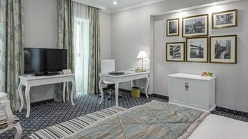 A hotel room with a bed, a TV, a desk with a lamp, a chair, and a cabinet. There are framed pictures on the wall.