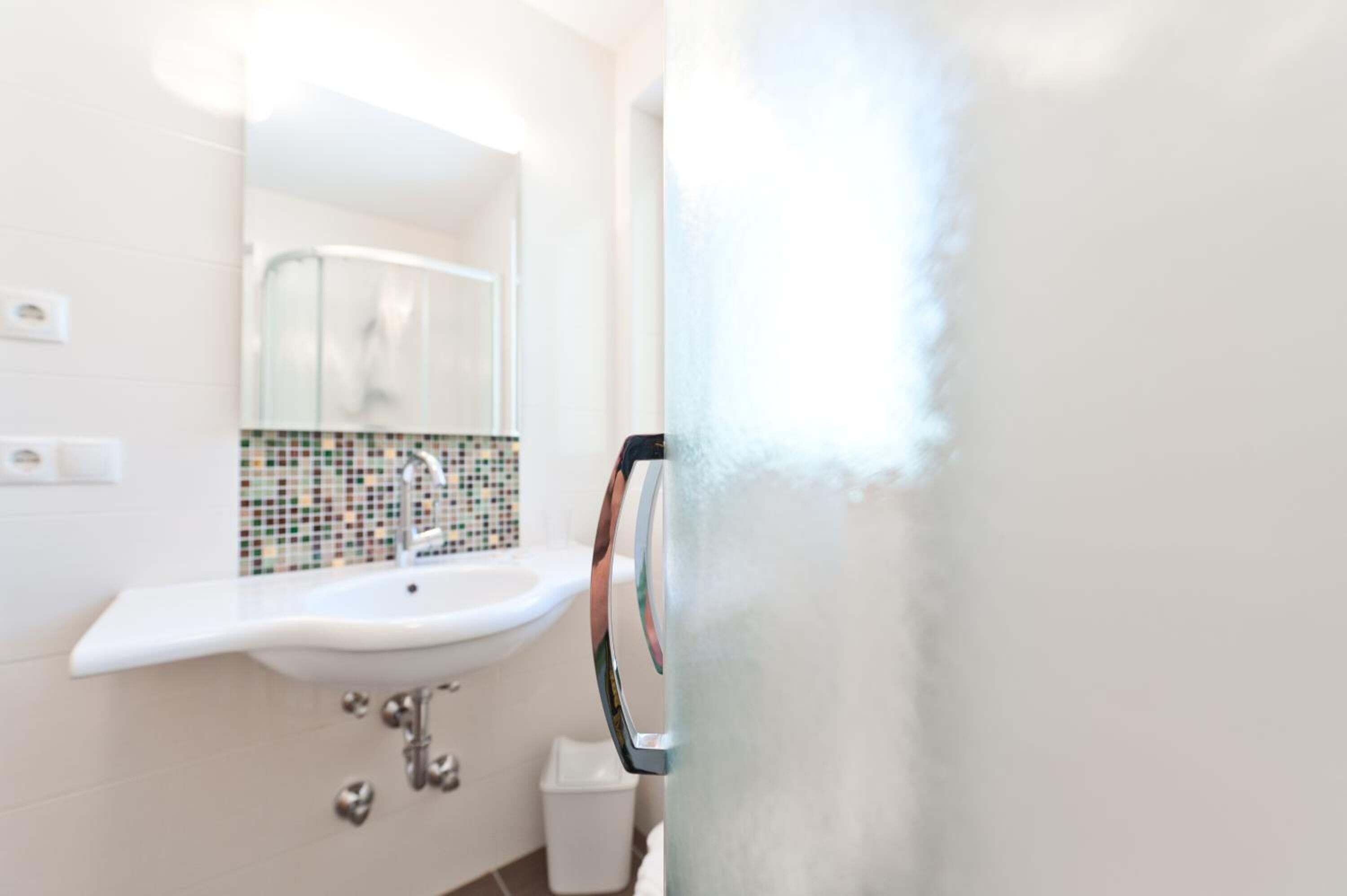 Een badkamer met een wit wastafelmeubel, een betegelde spatwand en een glazen douchecabine.