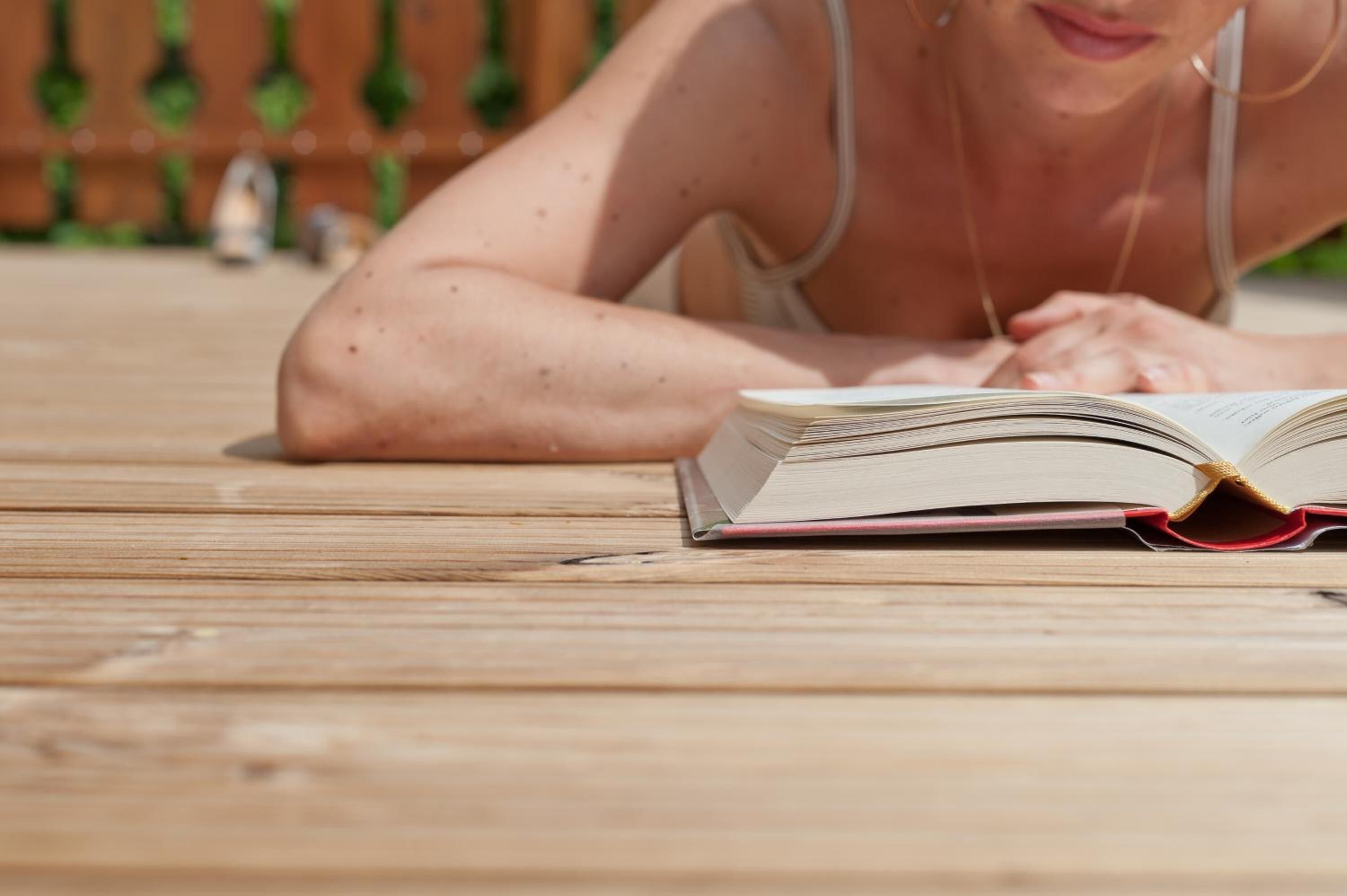 Une personne allongée sur une terrasse en bois, en train de lire un livre.