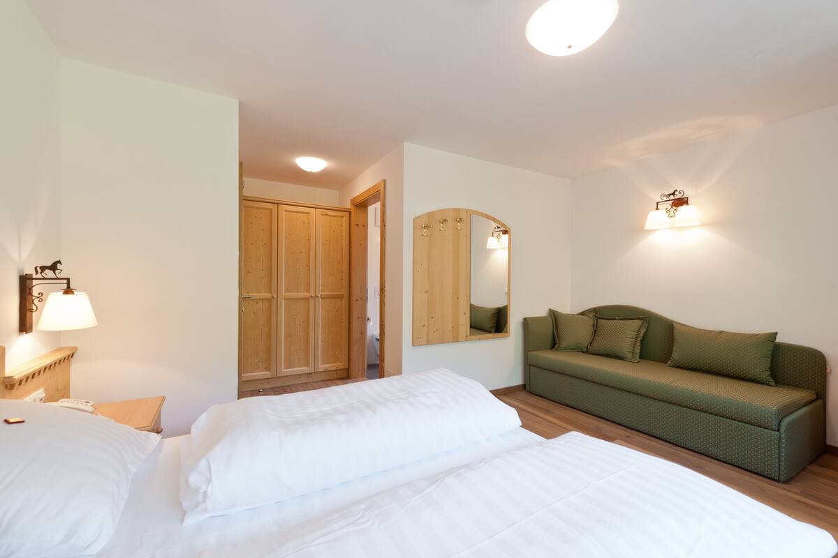 Ein Schlafzimmer mit einem Bett, einem grünen Sofa, einem Holzschrank und einem Spiegel.