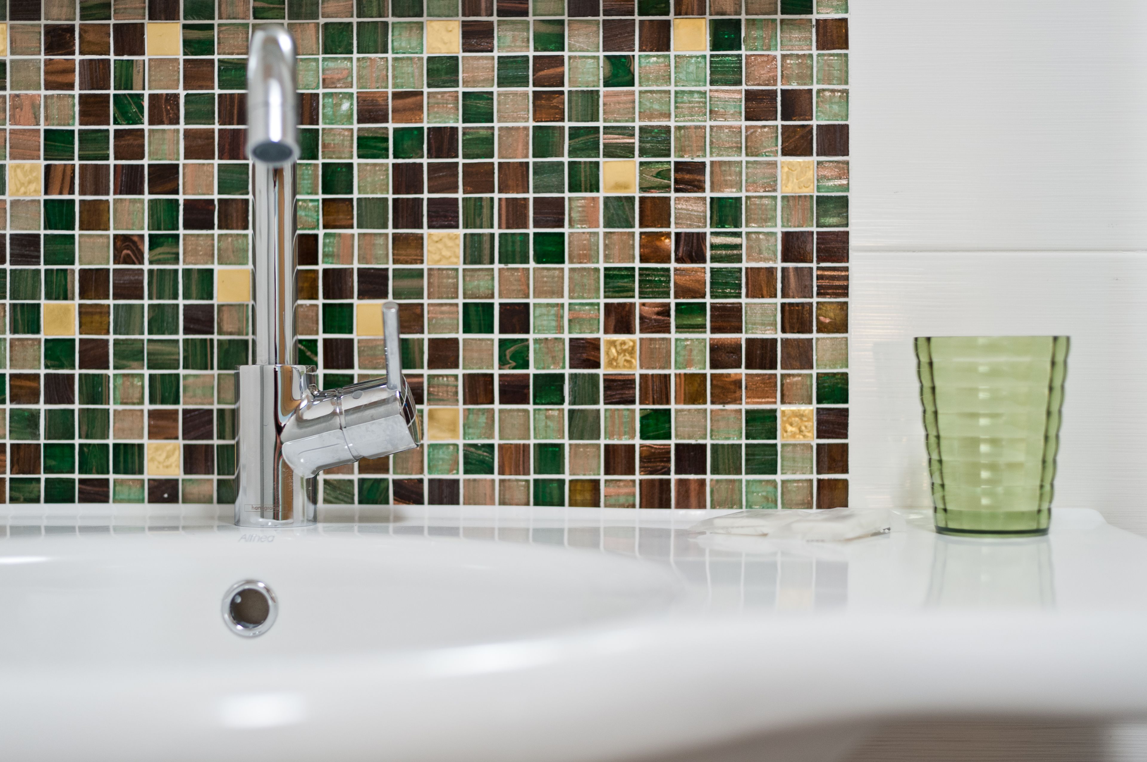 Ein Waschtisch mit modernem Wasserhahn und einer Rückwand aus Mosaikfliesen.