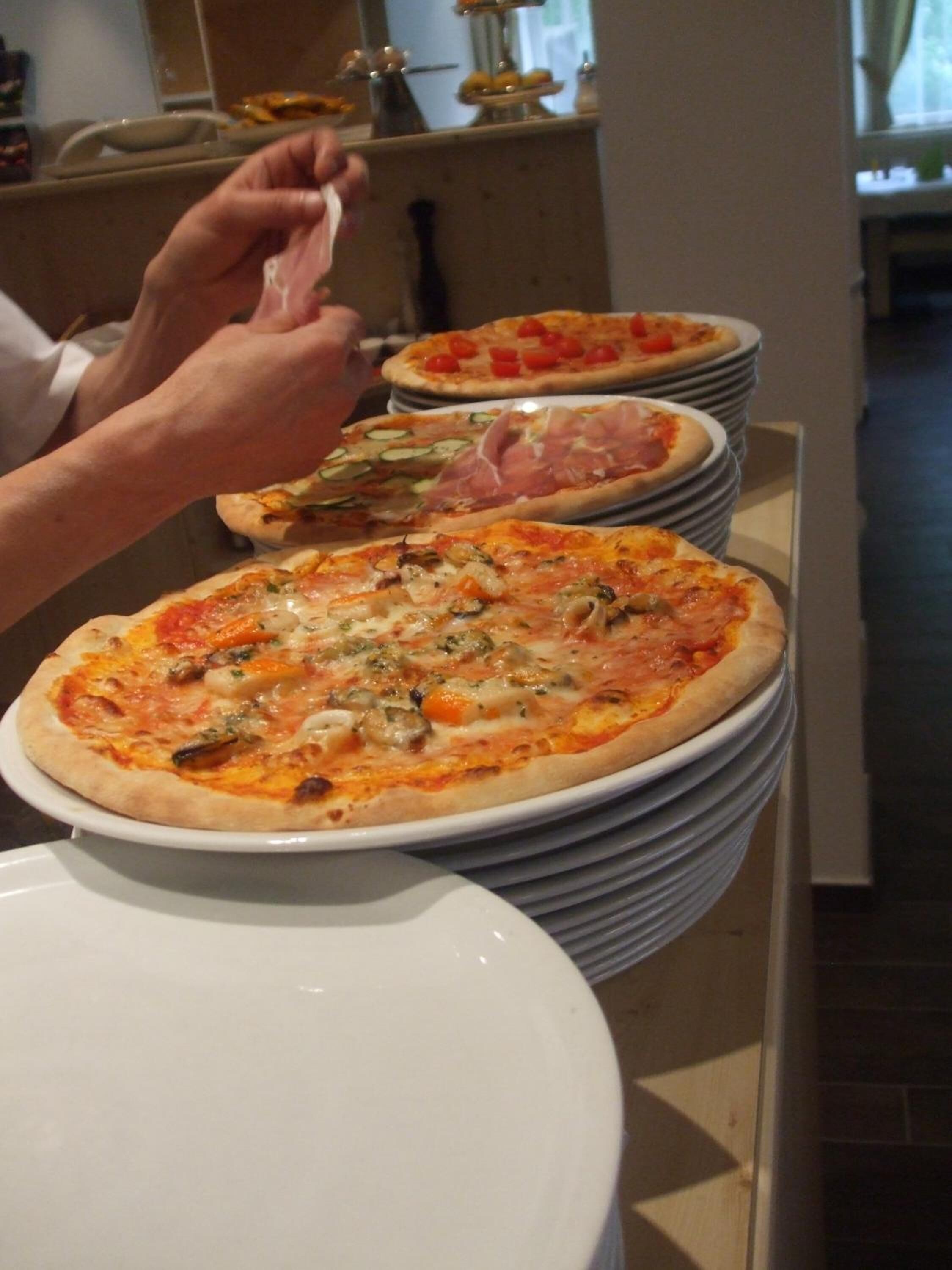 Variedad de pizzas sobre platos apilados en una cocina.