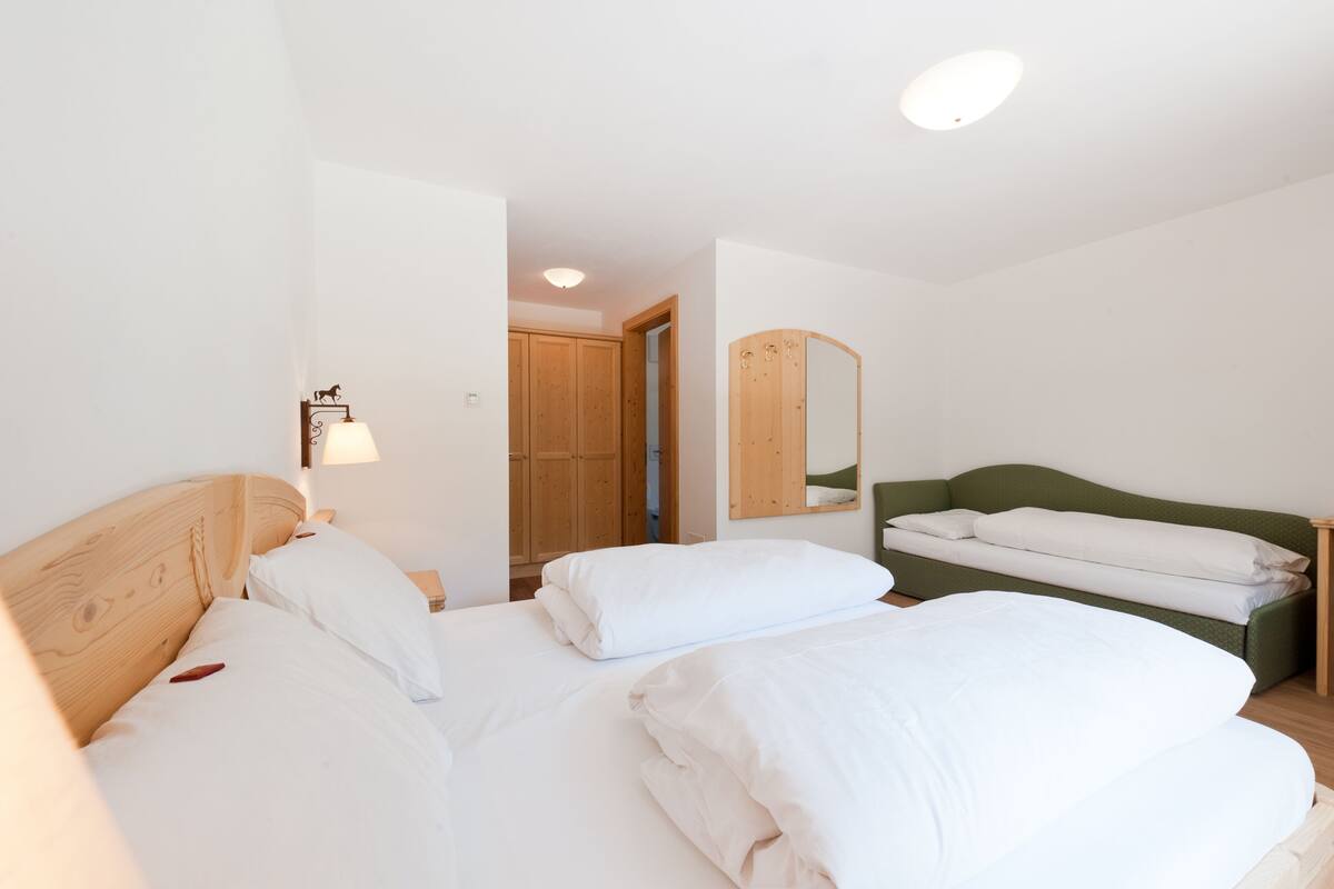 Ein Hotelzimmer mit einem Holzbett, einem grünen Sofa, einem großformatigen Spiegel und einem Holzschrank.