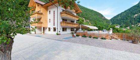 A multi-story hotel with balconies, a paved courtyard, and a mountainous backdrop.