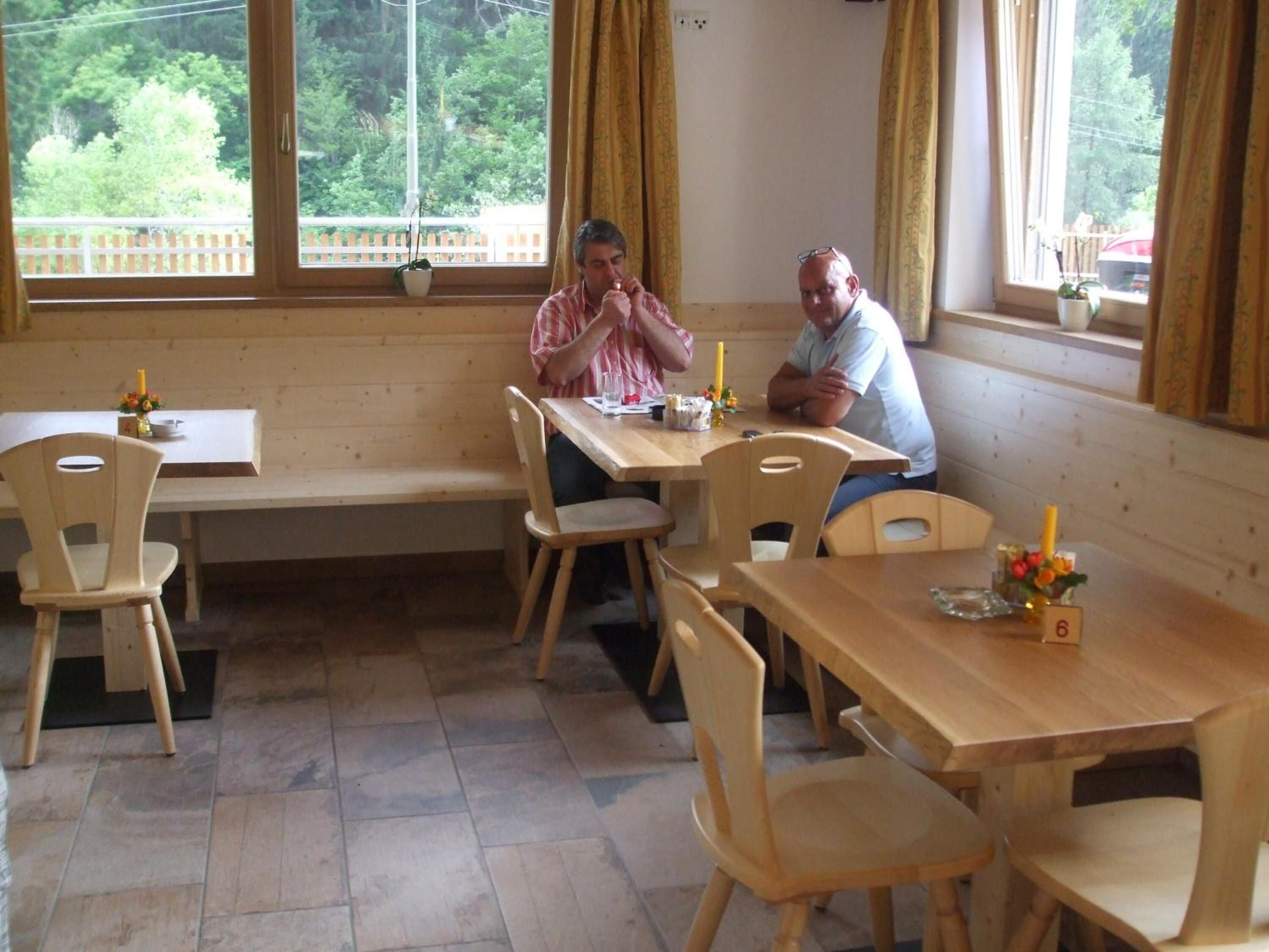 Comedor con mesas y sillas de madera, un banco y ventanas grandes con cortinas.