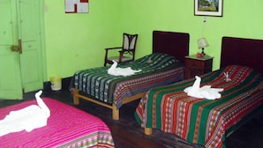 Una habitación con dos camas, cada una con un almohadón con forma de cisne, una silla, una mesita con l ámpara e imagen en la pared.