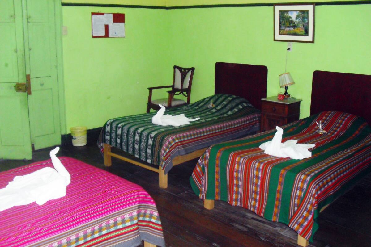 A room with two beds, each with a swan-shaped pillow, a chair, a small table with a lamp, and a picture on the wall.